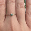 A close-up of a hand wearing a delicate gold ring with a small round green gemstone.